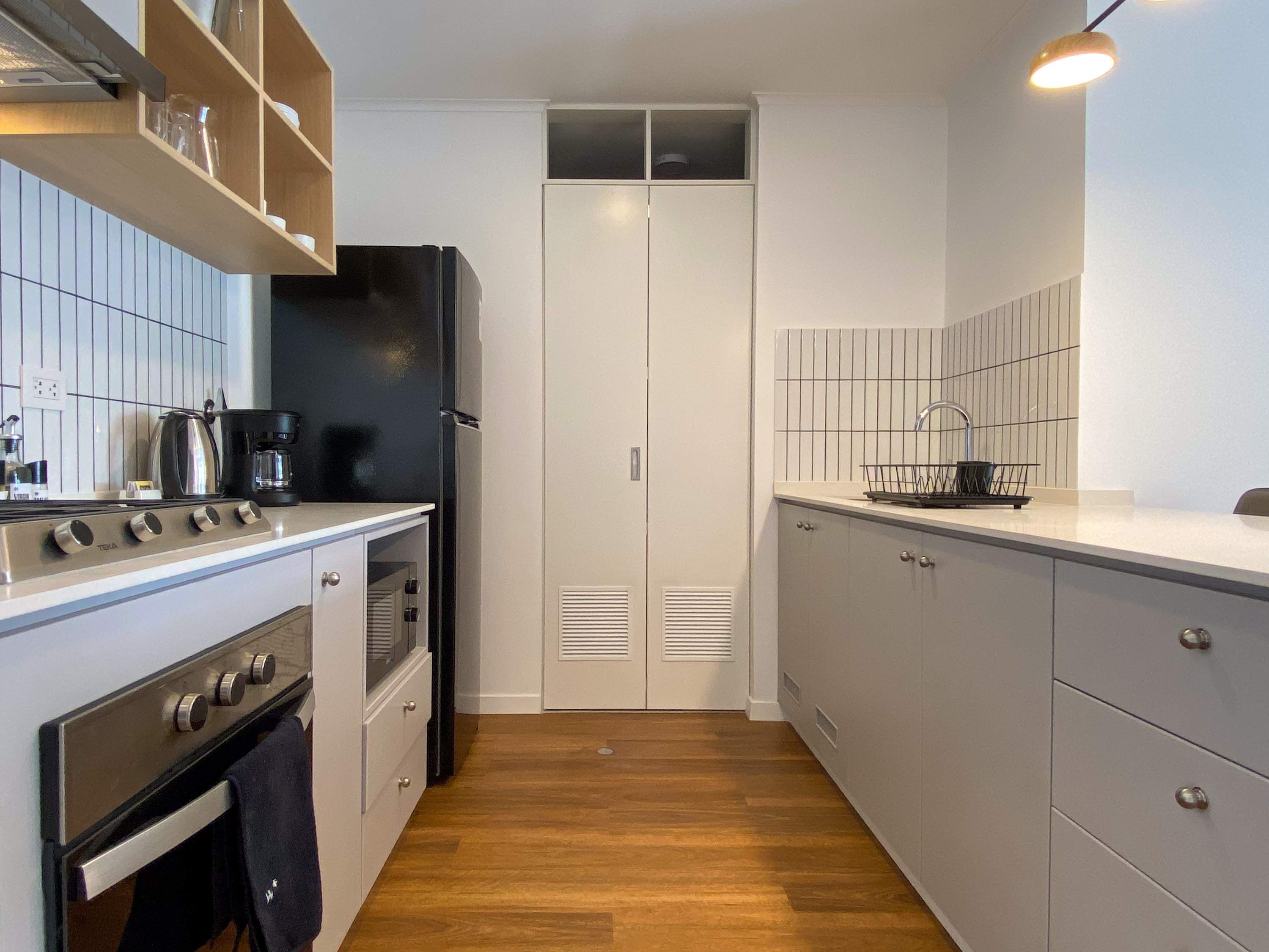 Een compacte keuken met een fornuis, oven en koelkast, houten kastjes en een betegelde spatwand.