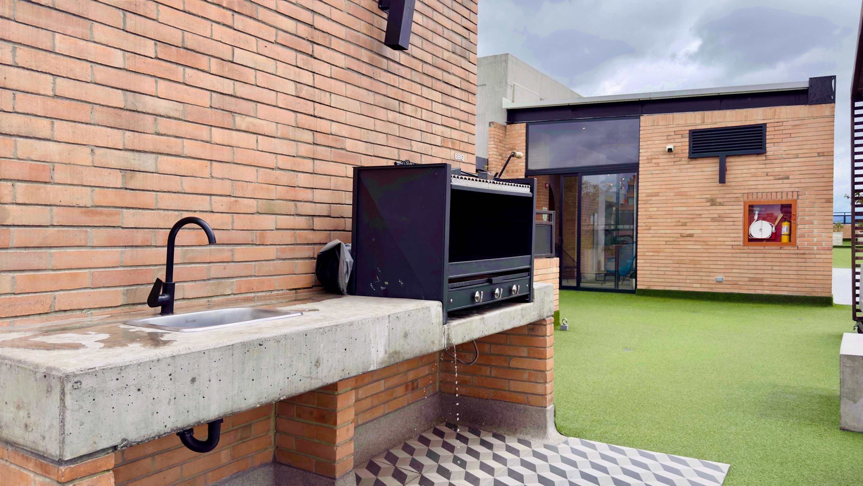 Une cuisine extérieure équipée d’un barbecue, d’un évier et d’un espace patio recouvert d’un gazon synthétique.