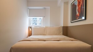 Ein ordentlich bezogenes Bett mit Kopfteil, ein Fenster mit Blick auf Gebäude und ein gerahmtes Bild an der Wand.