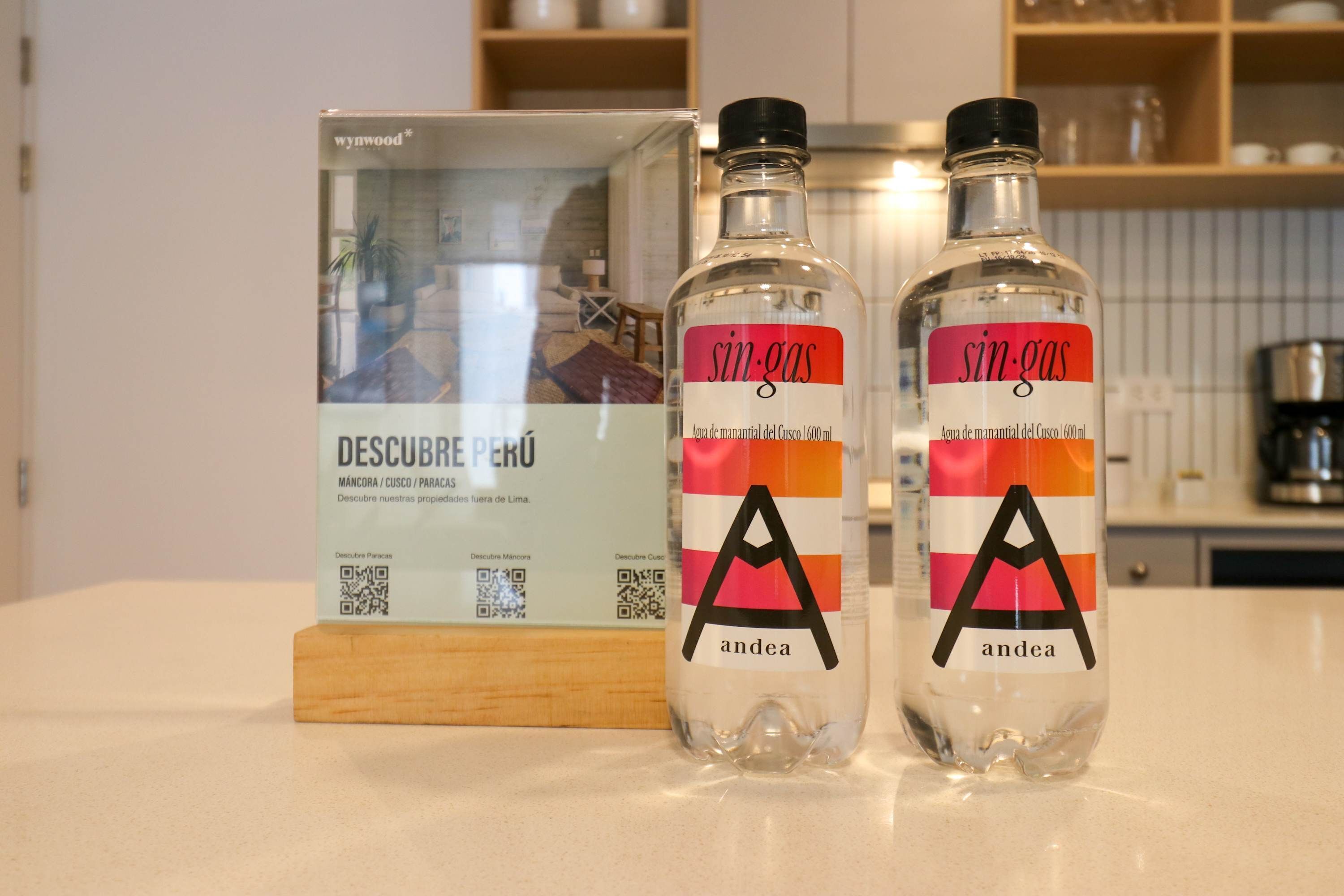 Two bottles of 'sin-gas' water with a QR code and a box labeled 'DESCUERDE PERU'.