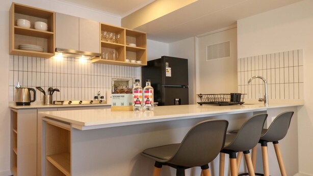 Eine moderne Küche mit einer zentralen Kochinsel, Barhocker, einem schwarzen Kühlschrank und Holzregalen.