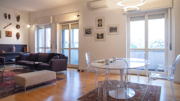 A modern living room with a sofa, coffee table, and clear chairs around a round table. - Bright Ambrose I Elegant 3 Bedroom Apartment With Balconies in Milan (Milan)