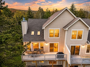 A two-story house with a deck, large windows, and a chimney. - Camelback Ski Retreat · Arcade + Games + Fireplace (Tannersville)
