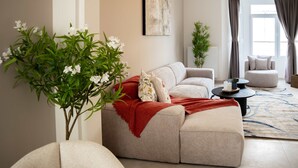 Uma sala de estar com sofá, mesa de centro, planta em vaso e janela com cortinas.