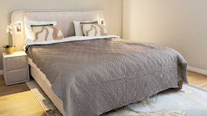 Quarto com cama, mesas de cabeceira, uma obra de arte na parede e um abajur.