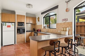 A kitchen with wooden cabinets, a central island with bar stools, a microwave, and a stove. - Group stays for Friends, Families, Weddings and Events. Walkable to Fremantle (Fremantle)