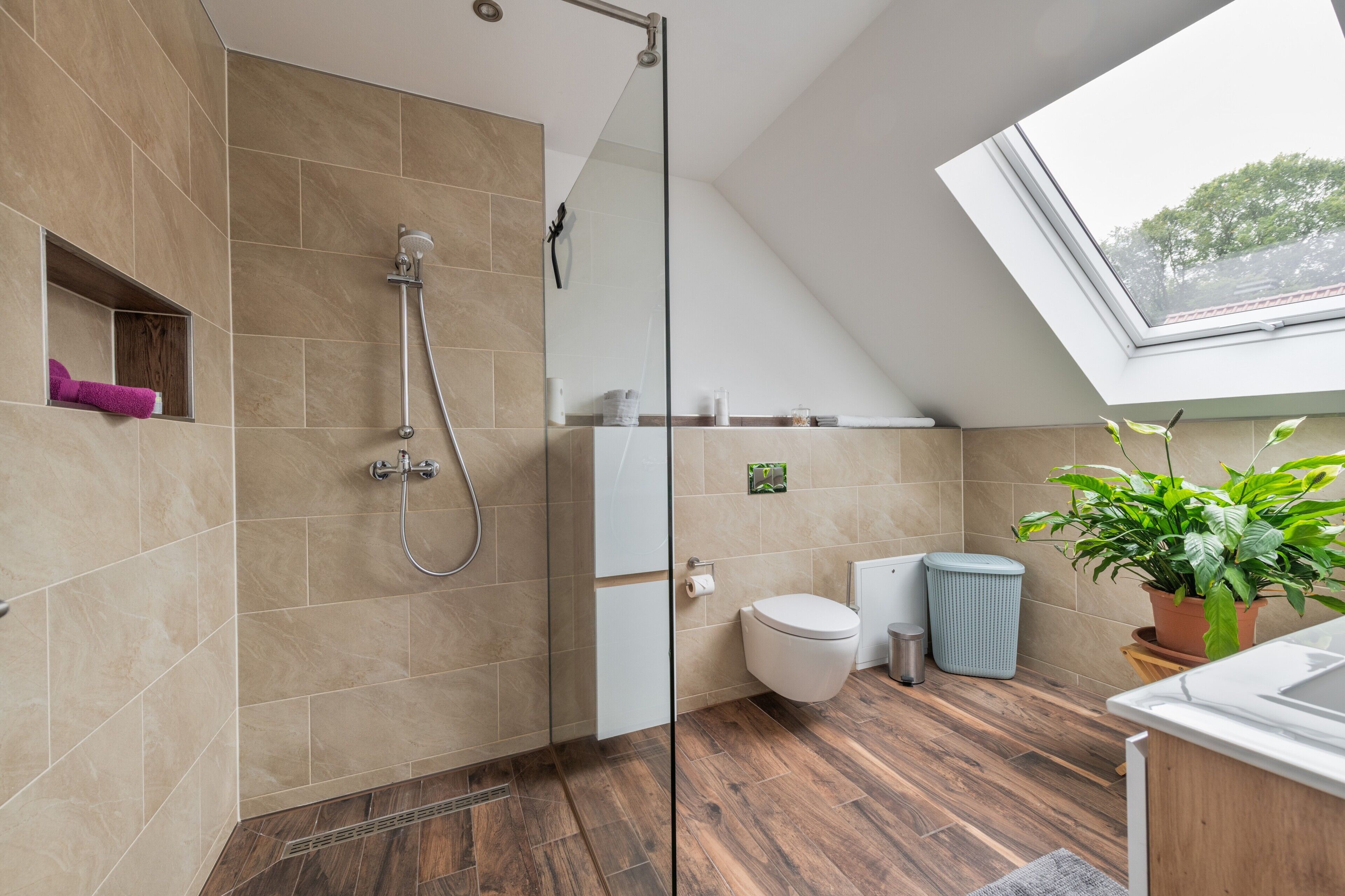 Une salle de bain moderne avec douche, toilettes et une fenêtre de toit.