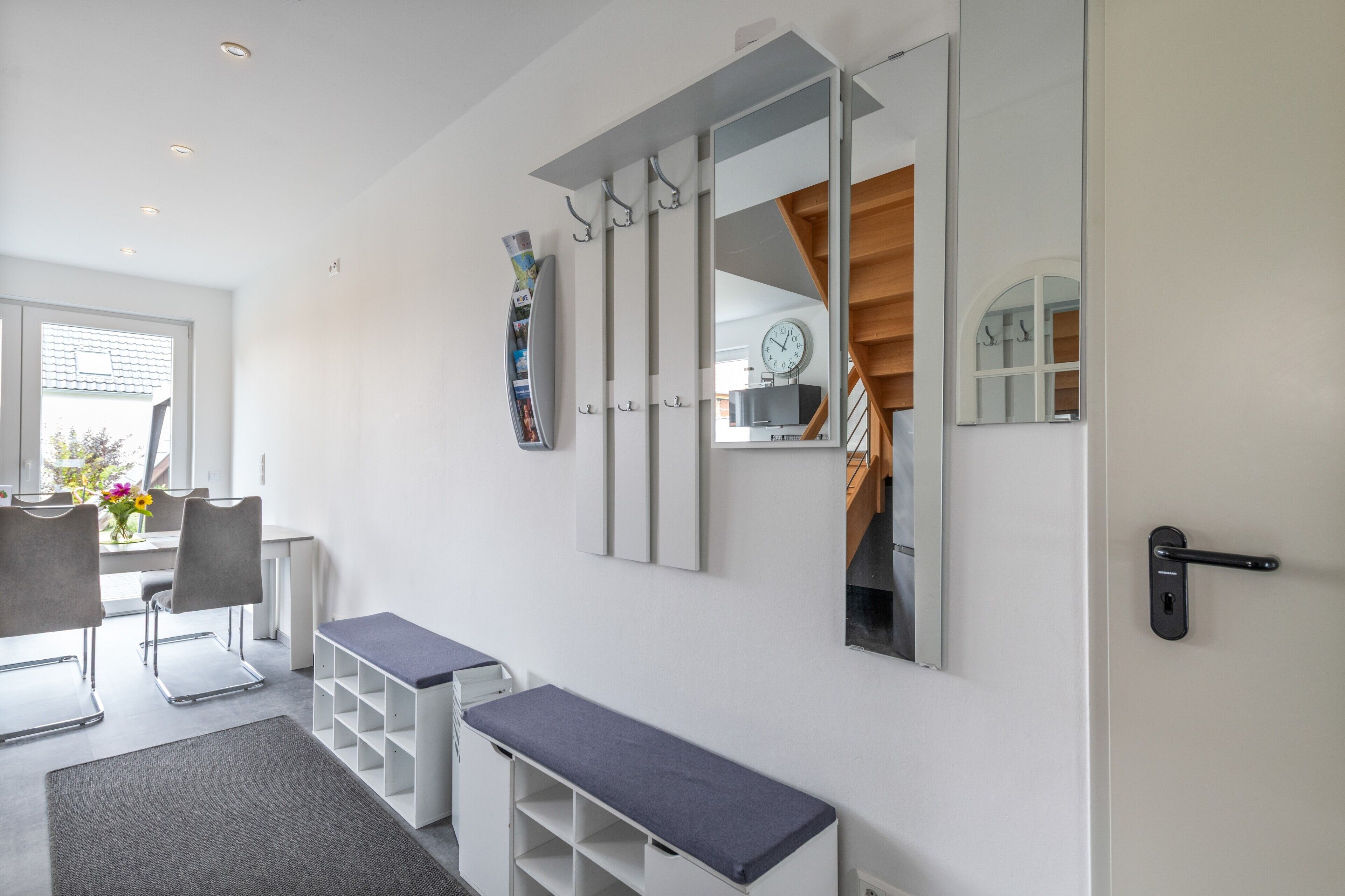 Un intérieur moderne comprenant un espace salon, un banc, un miroir et une porte dotée d’une poignée.