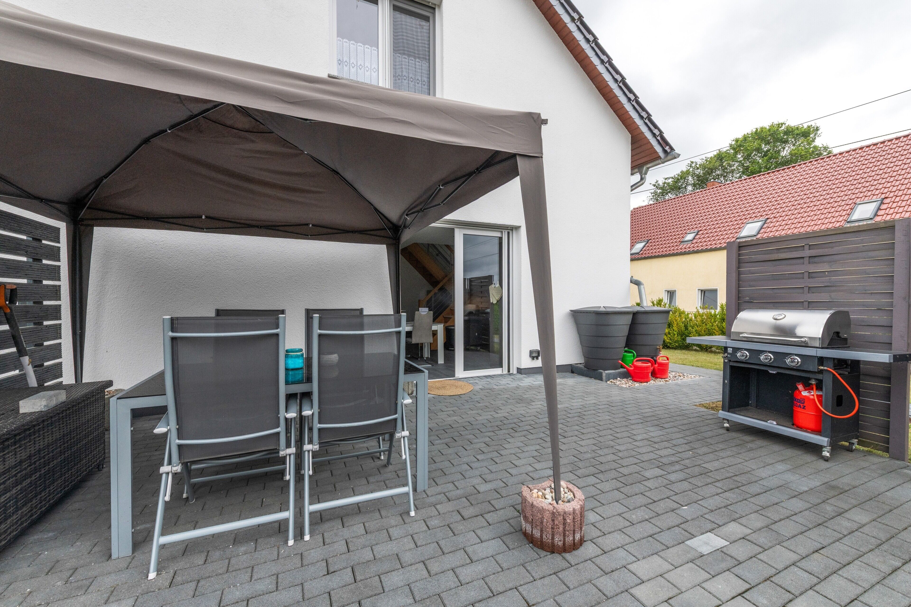 Eine Terrasses mit überdachtem Tisch und Stühlen, einem Grill und einem Boden aus Ziegelsteinen.