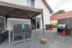 An outdoor patio with a covered table and chairs, a barbecue grill, and a brick floor. - Holiday Home 'Kronseeliebe' with Private Terrace, Garden, and Wi-Fi (Lychen)