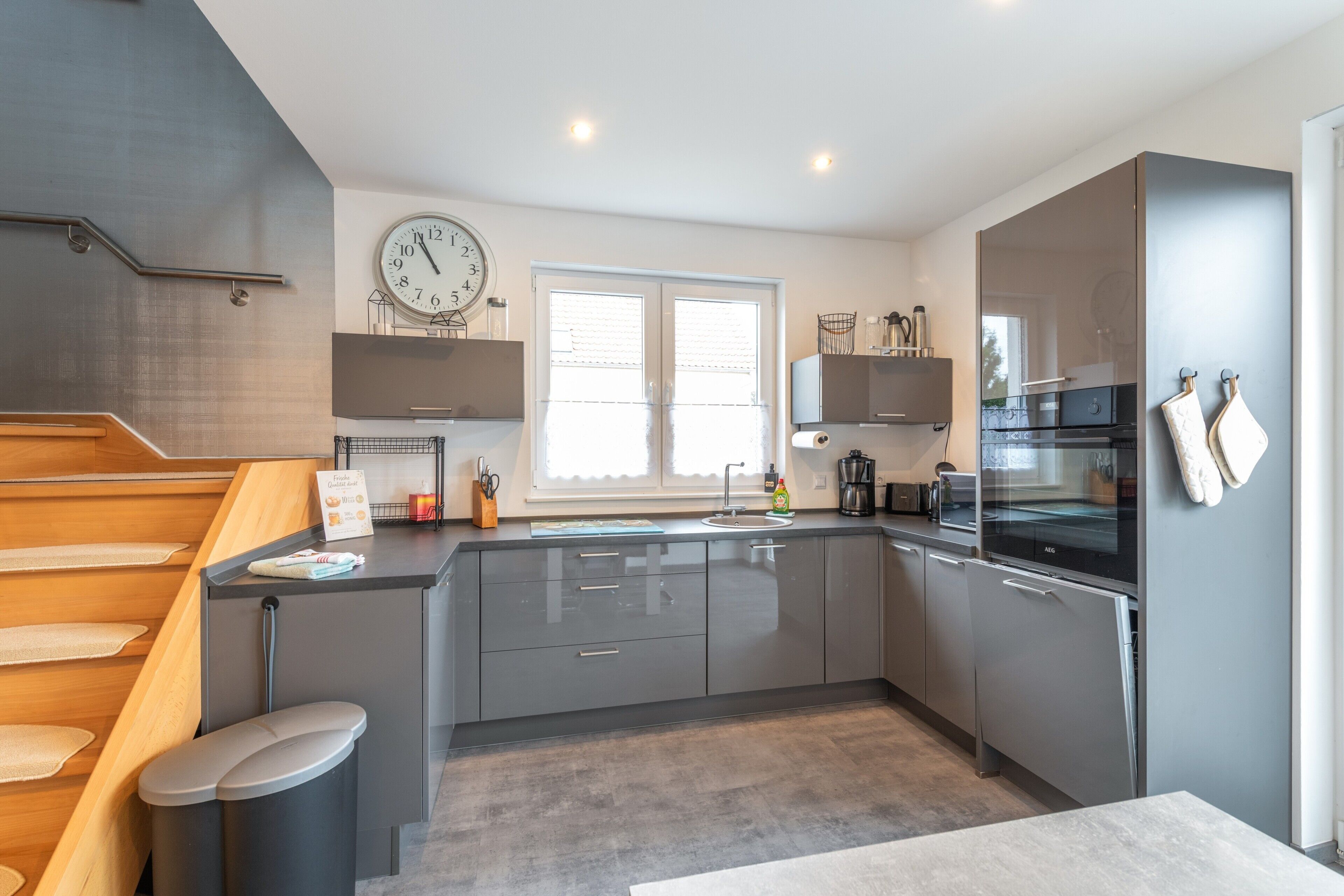 Een moderne keuken met grijze kastjes, een roestvrijstalen koelkast, een inbouwoven en een raam voor natuurlijk licht.