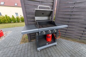 Una parrilla portátil de barbacoa con tanque de gas y perillas de control, ubicada sobre una superficie pavimentada.
