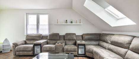 Un salon moderne avec un canapé d’angle, une table basse en verre et une lucarne.