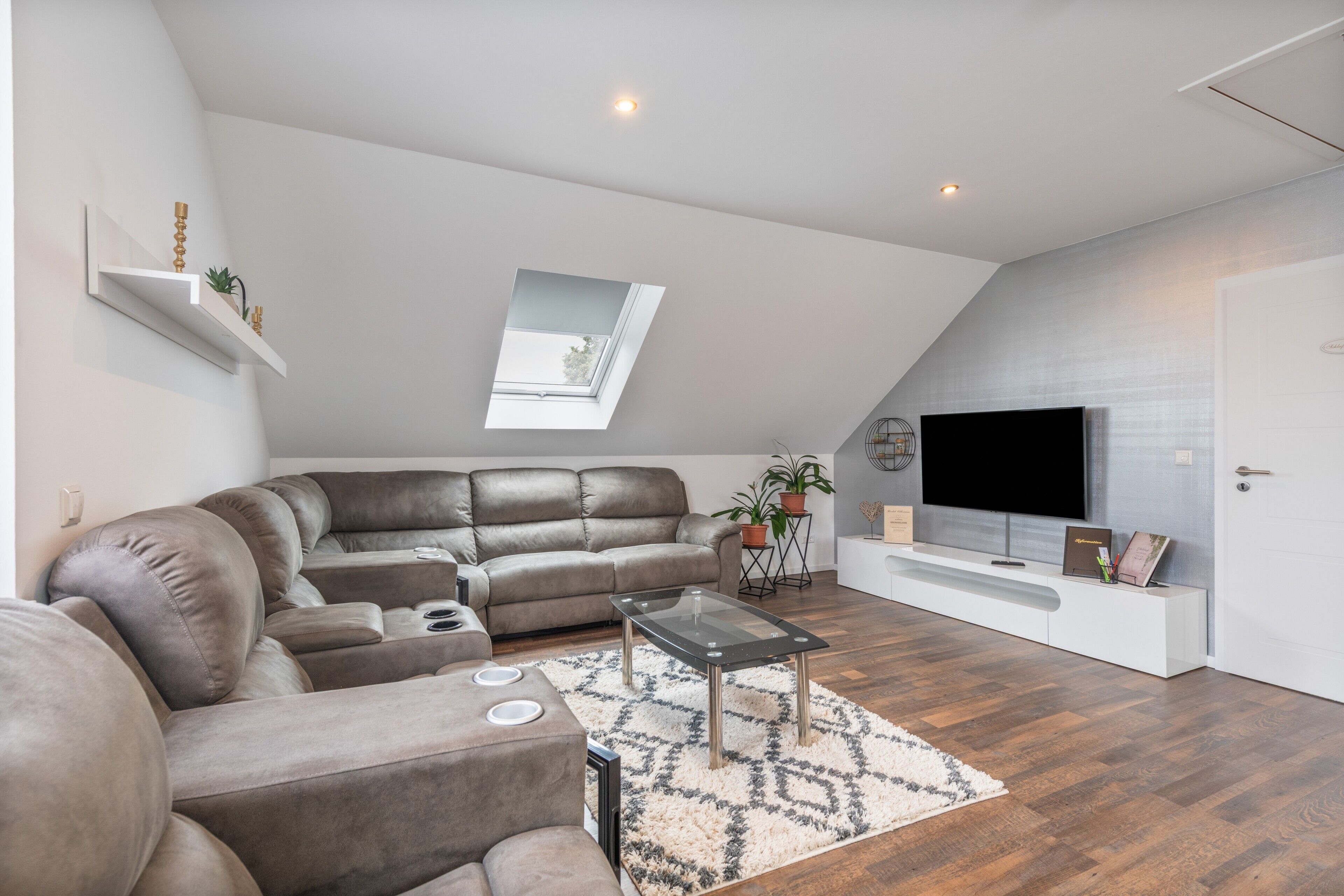 En moderne stue med en hjørnesofa, et fladskærms-tv og et ovenlys.