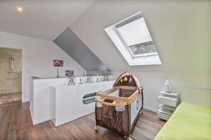 A modern, well-lit room with a sloped ceiling, a small window, a baby crib, a shower area, and a white reception desk. - Holiday Home 'Kronseeliebe' with Private Terrace, Garden, and Wi-Fi (Lychen)