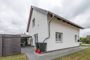 A two-story house with a white exterior, a grey roof, and a grey gutter system. There is a small shed to the left and a paved driveway leading to the house. - Holiday Home 'Kronseeliebe' with Private Terrace, Garden, and Wi-Fi (Lychen)