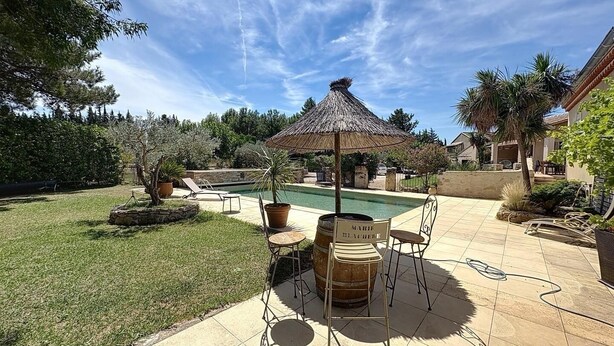 Patio con piscina, una sombrilla de paja y mobiliario de exterior.