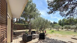Una terraza de madera con mobiliario exterior, una pérgola y árboles al fondo.