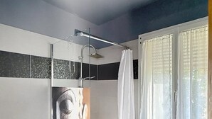 Un baño con cabina de ducha de vidrio, inodoro, lavabo y ventana con cortinas.