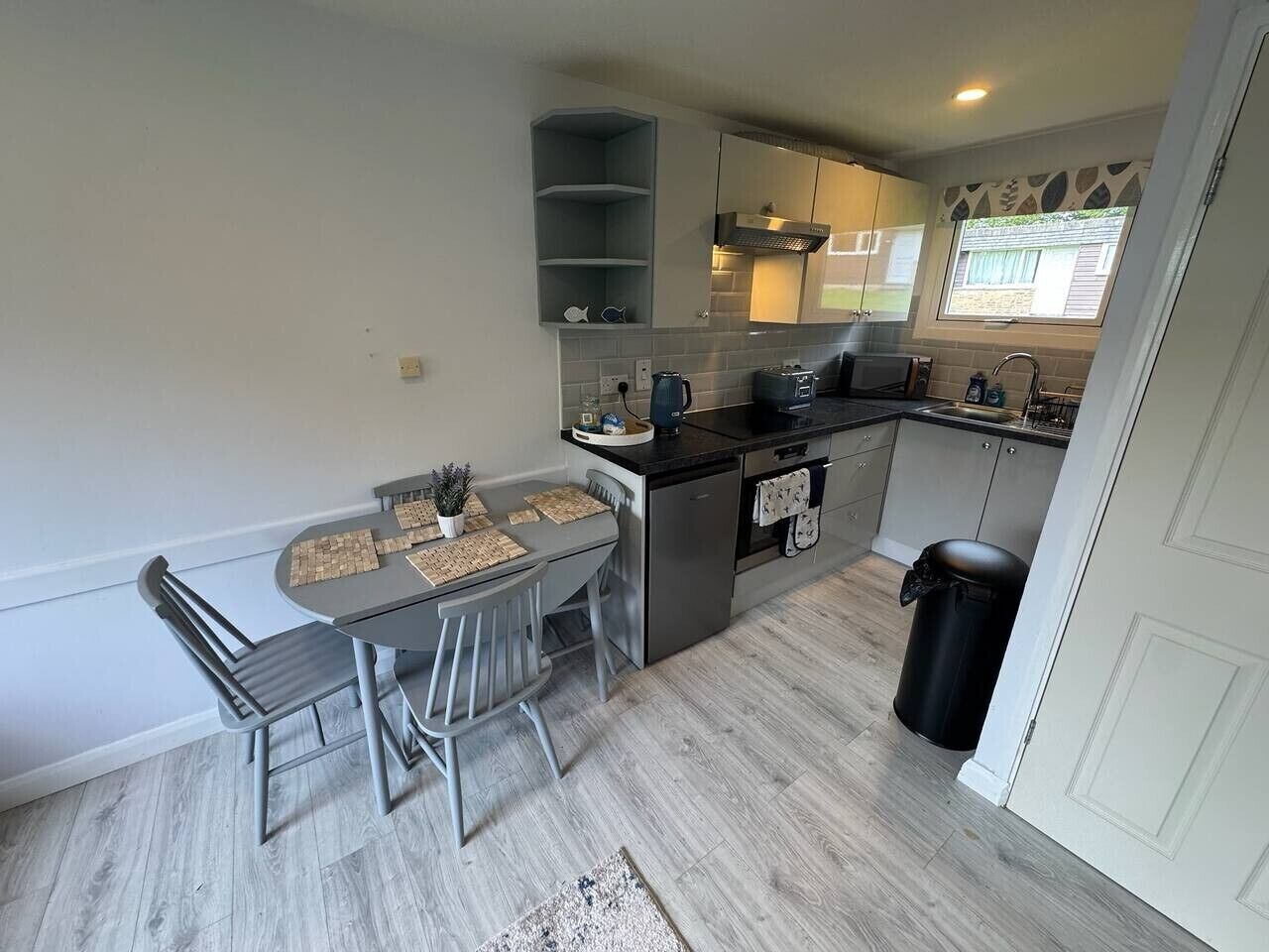 A compact kitchen with a dining table, chairs, a sink, and a trash bin.