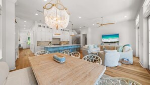 Une cuisine moderne avec des meubles blancs, une table à manger en bois et un grand lustre.