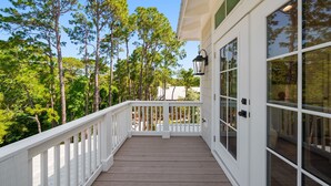Une terrasse en bois avec une balustrade blanche, de grandes fenêtres et une vue sur de grands pins.