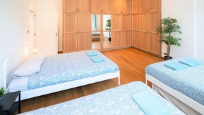 A bedroom with two beds, wooden wardrobes, a potted plant, and a view into another room. - 3 Bedroom Cosy Apartment (Antwerp)