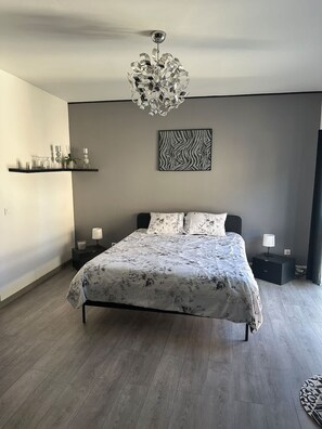 Ein Schlafzimmer mit einem Bett, einer Hängelampe, einem Wandbild und einem Regal mit Dekoration.