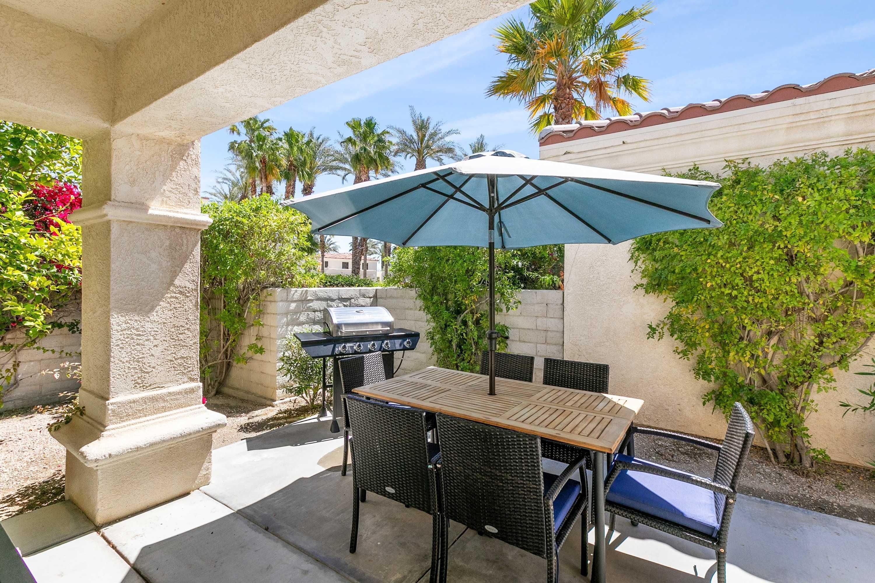 Une terrasse extérieure avec une table et des chaises, un barbecue et un parasol.