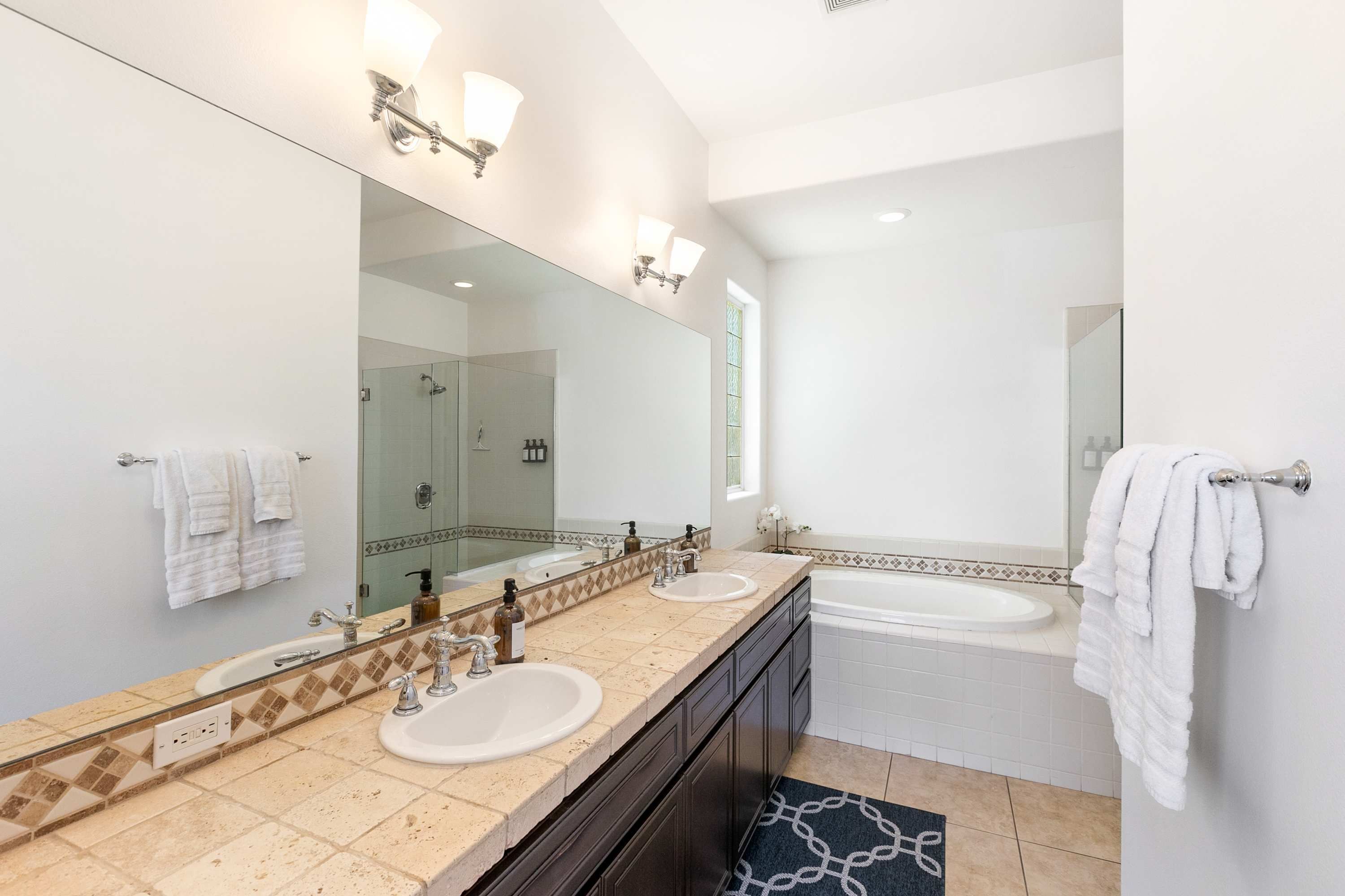 A modern bathroom with two sinks, a large mirror, and a bathtub.