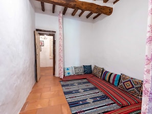 Un pasillo estrecho con suelo de baldosas que conduce a una habitación con techo bajo y vigas de madera a la vista.