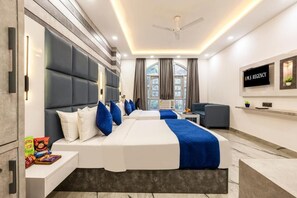 A modern hotel room with a large bed, a desk, a chair, a TV, and a window with curtains. - MS REGENCY (New Delhi)