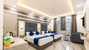 A hotel room with two beds, a desk, a chair, a TV, and a window with curtains. - MS REGENCY (New Delhi)
