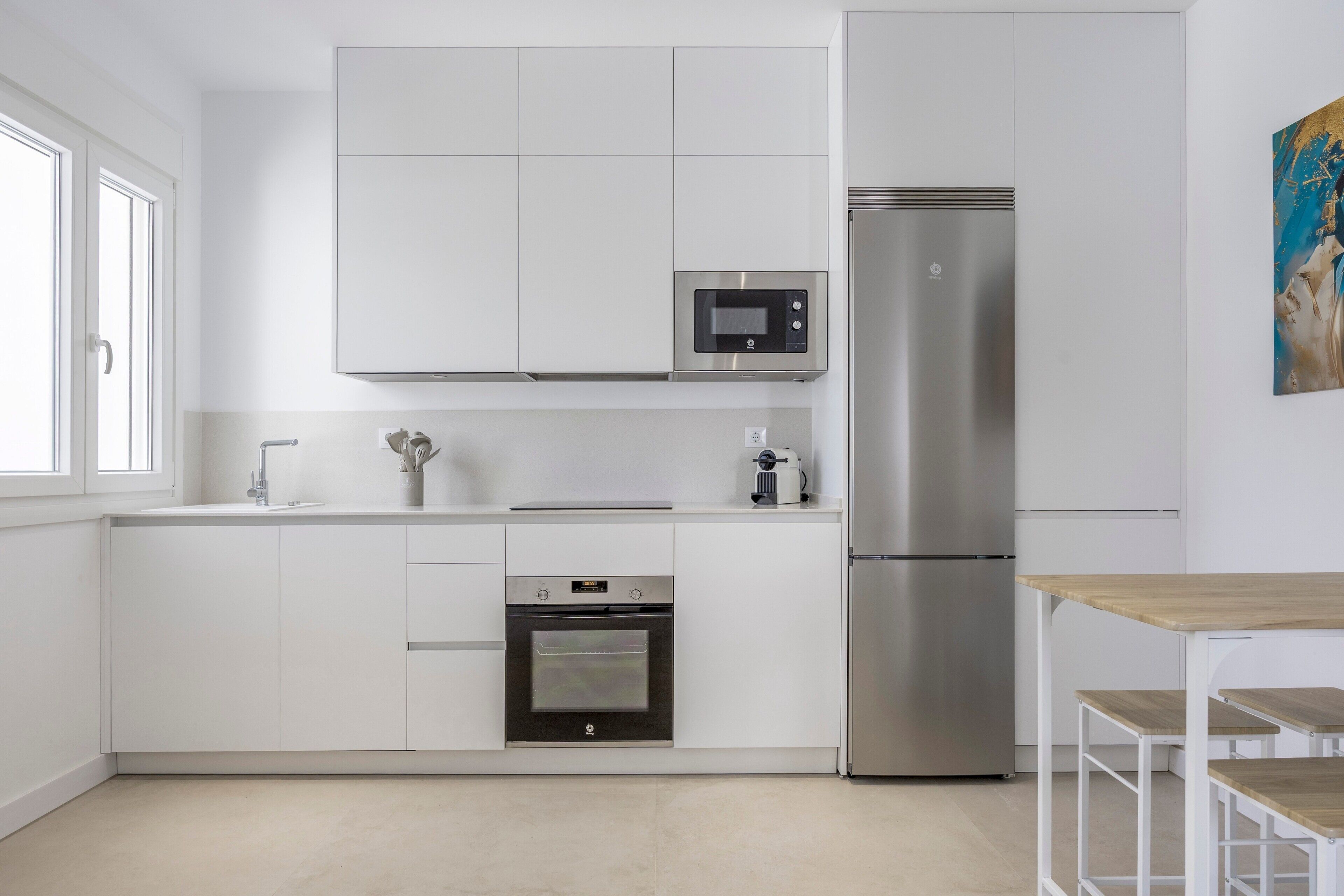 A modern kitchen with white cabinetry, a stainless steel refrigerator, a microwave, and an oven.