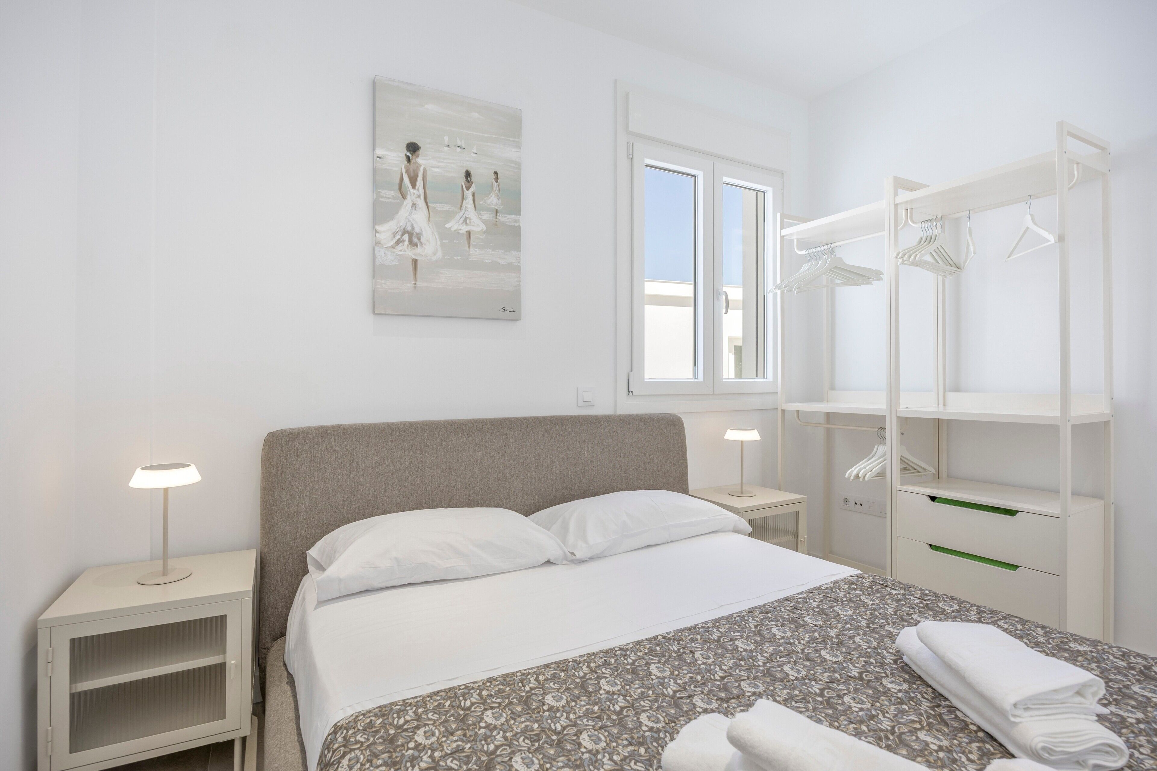 Una camera da letto con un letto, comodini, una finestra, un armadio e un quadro appeso al muro.