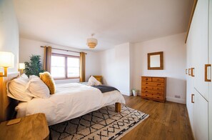 Ein Schlafzimmer mit Bett, Nachttisch, Schminktisch und einem Fenster mit Vorhängen.