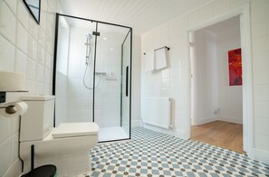 Ein Badezimmer mit Duschkabine aus Glas, Toilette, einem Musterfliesenboden und einem weißen Heizkörper.