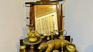 Uma mesa de madeira com objetos de latão, incluindo uma grande estátua de elefante, um espelho e vários recipientes.