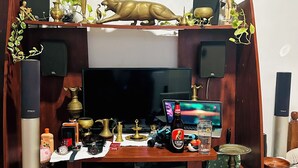 Quarto com televisão, alto-falantes e diversos objetos decorativos nas prateleiras.