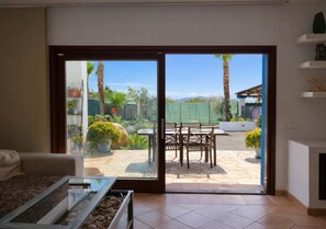 Ein Zimmer mit einer Schiebetür und einem Ausgang zur Terrasse, auf der sich ein Tisch und Stühle befinden.