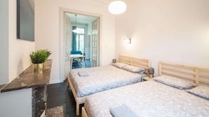 Ein Schlafzimmer mit zwei Betten, einem Schreibtisch, einem Stuhl, einer Topfpflanze und einer Pendelleuchte.