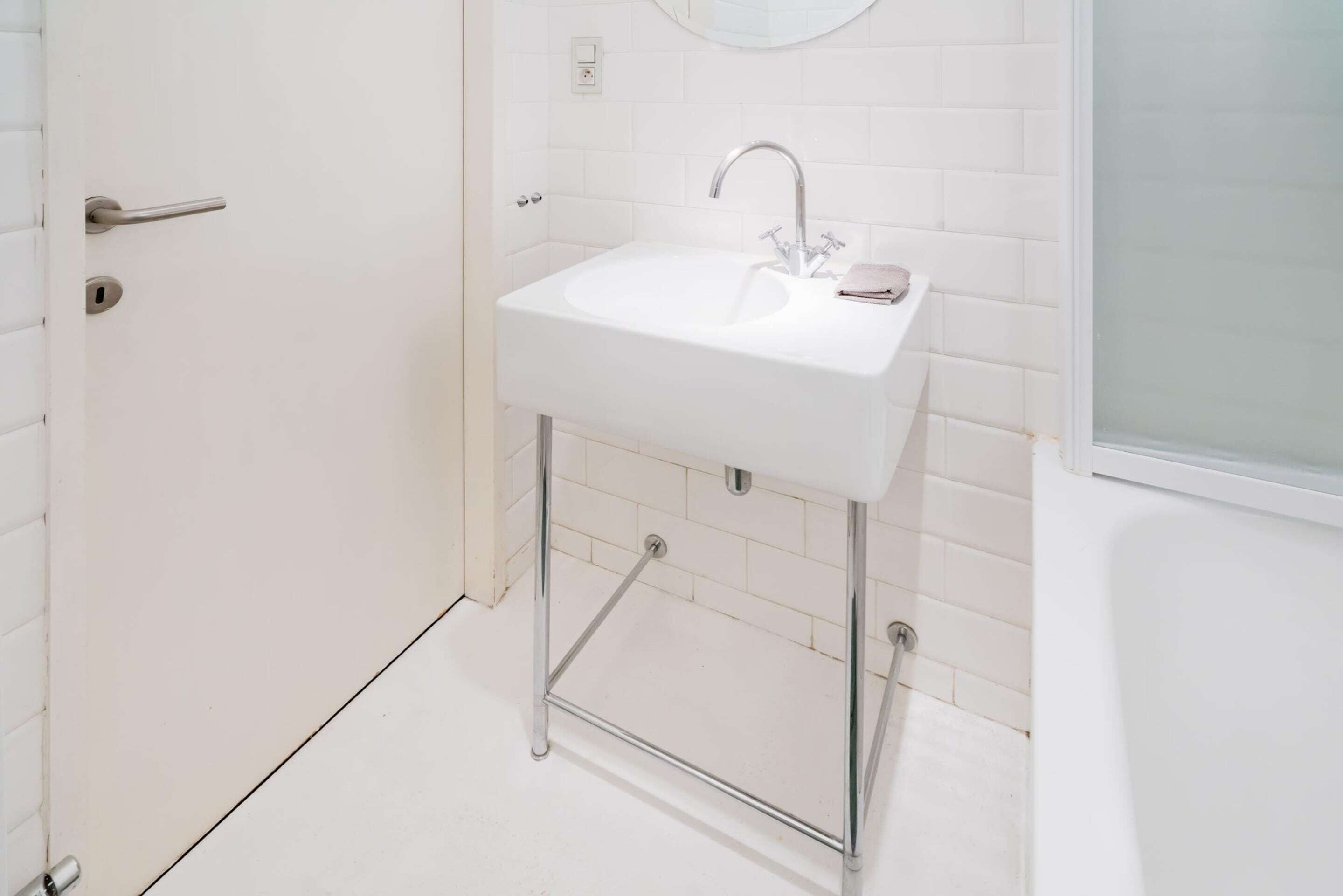 Un baño con un lavamanos blanco, grifo cromado y un espejo encima.