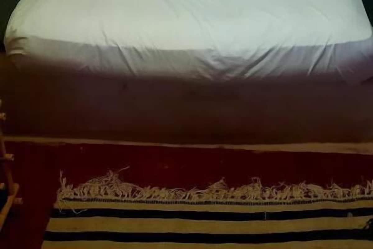 A bed with white bedding, a headboard with a geometric design, and a striped rug.