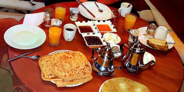 Una escena de desayuno con panes planos, té y diferentes salsas sobre una mesa de madera.