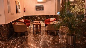 A lobby with marble flooring, red and beige chairs, a small round table, and a potted plant. - Quiet Rooms 14  (Riyadh)