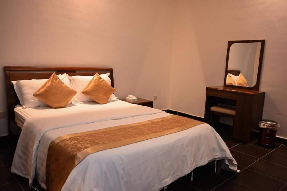A neatly made bed with a wooden headboard, a bedside table with a lamp, and a mirror on the wall.