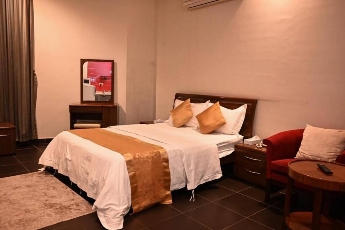 A hotel room with a bed, bedside table, chair, and a small round table.