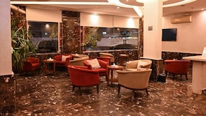 A hotel lobby with red and beige armchairs, a marble floor, a large pillar, and a view of the outside. - Quiet Rooms 14  (Riyadh)