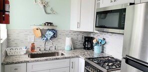 A kitchen with a granite countertop, stainless steel appliances, a gas stove, a microwave, and a sink. - Modern Beach Retreat - Mermaid Cottage (St. Augustine)