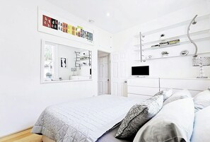 Ein Schlafzimmer mit einem Bett, einem Fernseher, einem Spiegel und Regalen mit Dekoration.